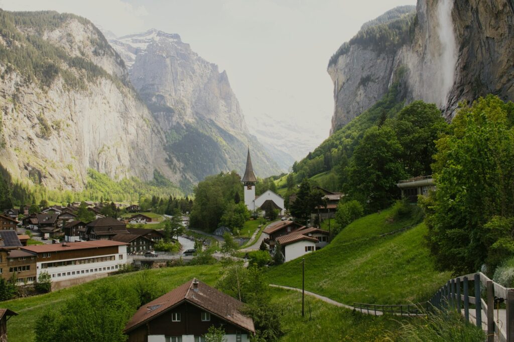 A scenic village sits amidst towering mountains and waterfalls.